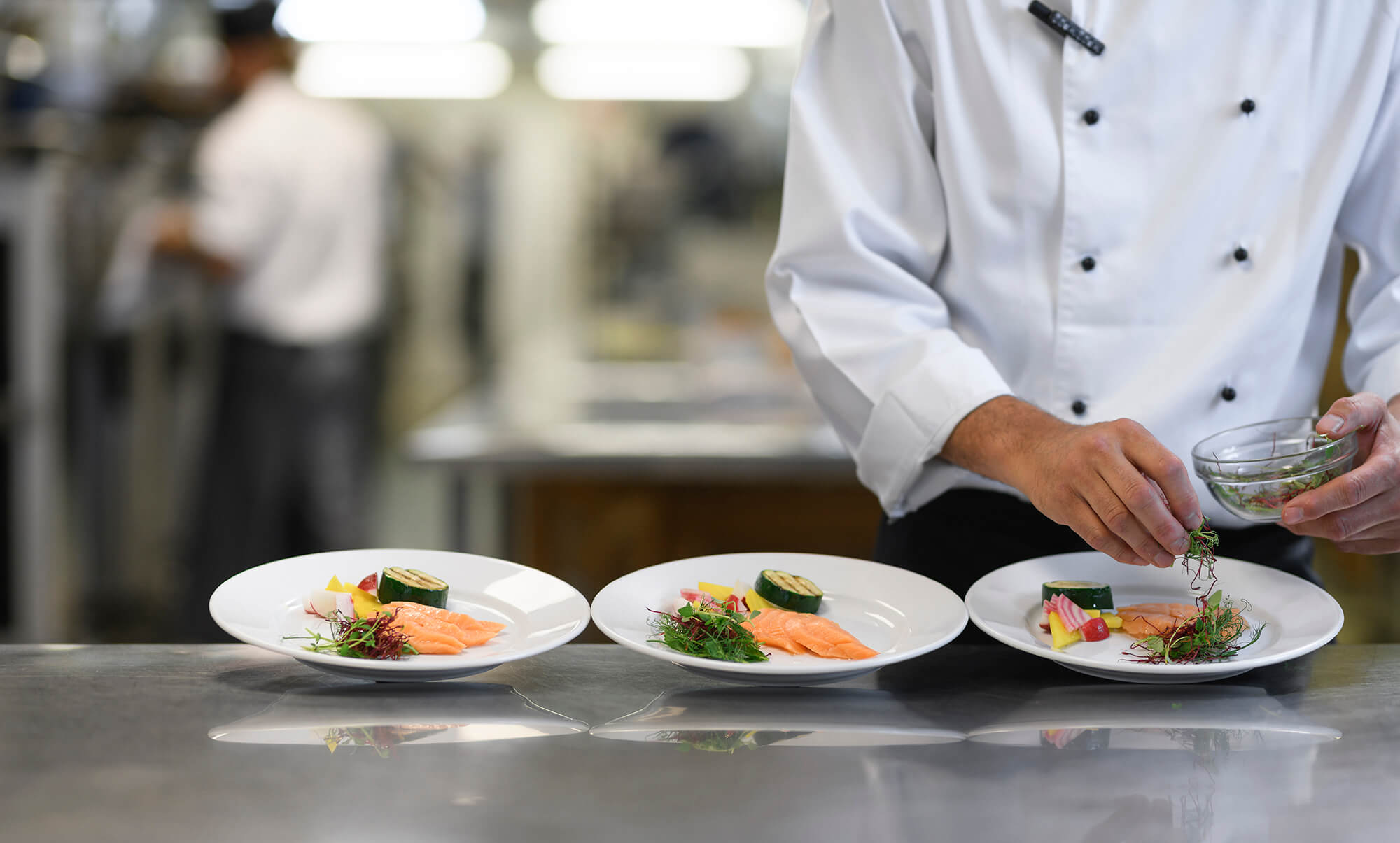 En kock lägger upp mat på tre tallrikar
