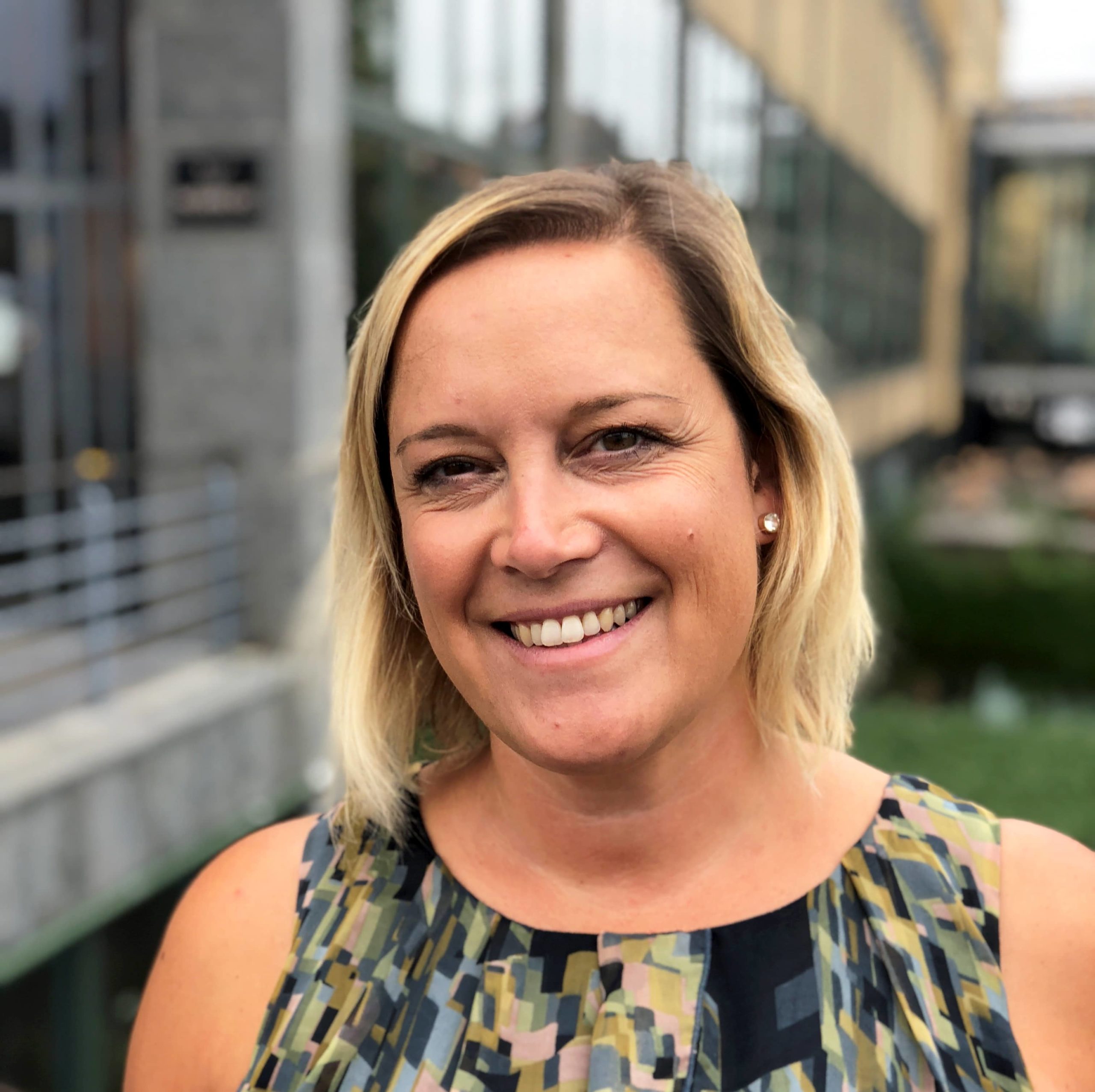 En kvinna med ljust axellångt hår ler in i kameran