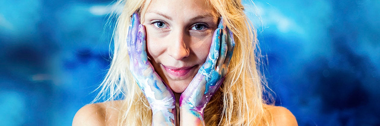 Kvinna håller händerna i ansiktet, händerna är fyllda av färg